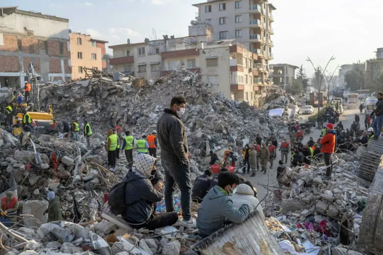 Pessoas caminham sobre os escombros de prédios desabados em meio a operações de resgate em Hatay, Turquia

 (AFP/AFP)