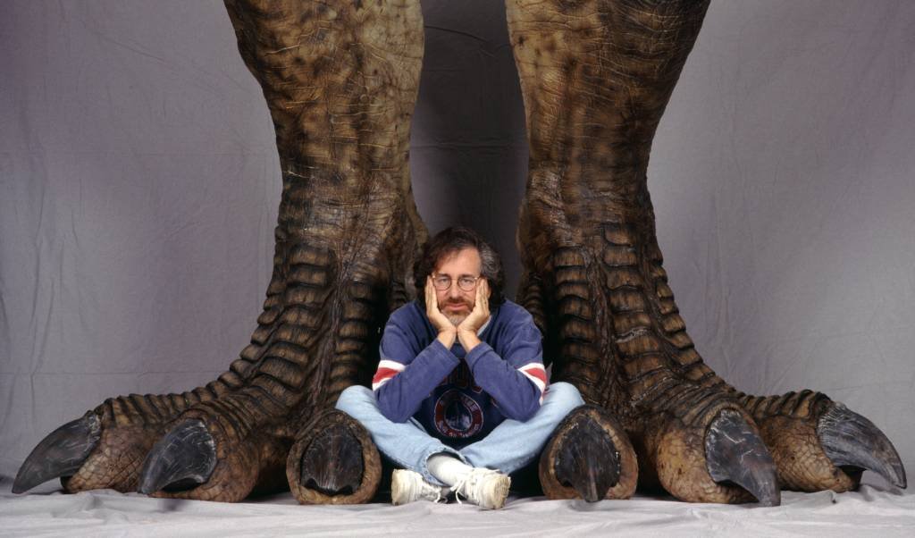 O diretor americano Steven Spielberg posa entre um par de pés gigantes de dinossauro em uma foto publicitária do filme 'Jurassic Park', 1993. (Murray Close/Getty Images)