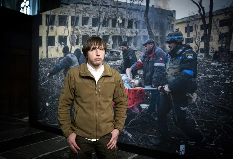 Vencedor do prêmio World Press Photo of the Year 2023, o fotógrafo ucraniano Evgeniy Maloletka, que trabalha para a Associated Press (AP), posa ao lado de sua foto vencedora no Nieuwe Kerk, em Amsterdã (AFP/AFP)