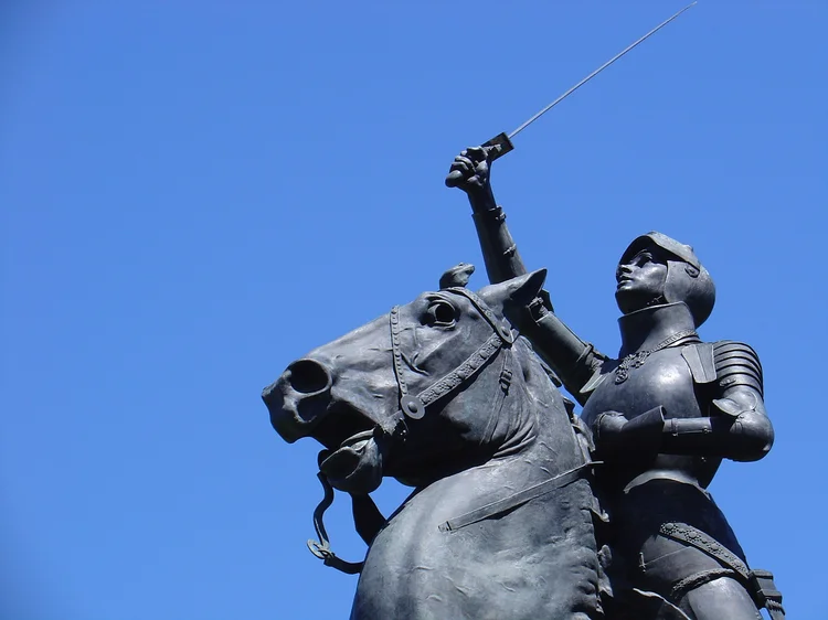 An old park statue from the late 1800's holds  up a sword up in an apparent show of victory.  The statue depicts a female riding a horse; she's rather like Joan of Arc. (Sparky2000/Getty Images)