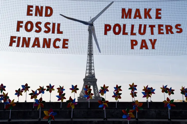 TOPSHOT - This photograph taken on June 21, 2023, shows a replica of a wind turbine on a net reading "End fossil finance, make polluters pay" as activists demonstrate against fossil finance on the Trocadero Plaza, with the Eiffel Tower in background in Paris, on the eve of the Summit for a New Global Financial Pact. (Photo by LUDOVIC MARIN / AFP) (Photo by LUDOVIC MARIN/AFP via Getty Images) (LUDOVIC MARIN/AFP/Getty Images)