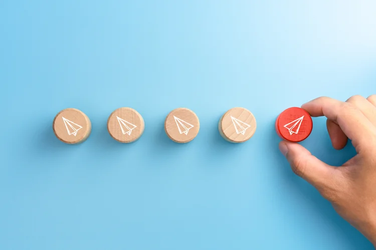 Businessman hand choose a red wood block with paper plane icons that are different from the group, blue background, Business concept for new ideas creativity and innovative solution, copy space (AdobeStock/Divulgação)