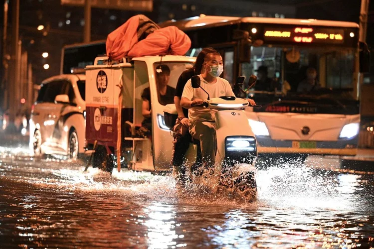 Commuters make their way through a flooded street after a rain shower in Beijing on August 4, 2022. (Photo by Noel Celis / AFP) (Photo by NOEL CELIS/AFP via Getty Images) (Photo by NOEL CELIS/AFP via Getty Images/Divulgação)