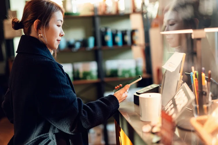 Young Asian woman making contactless mobile payment with smartphone at cafe. Financial technology and contactless payment concept.