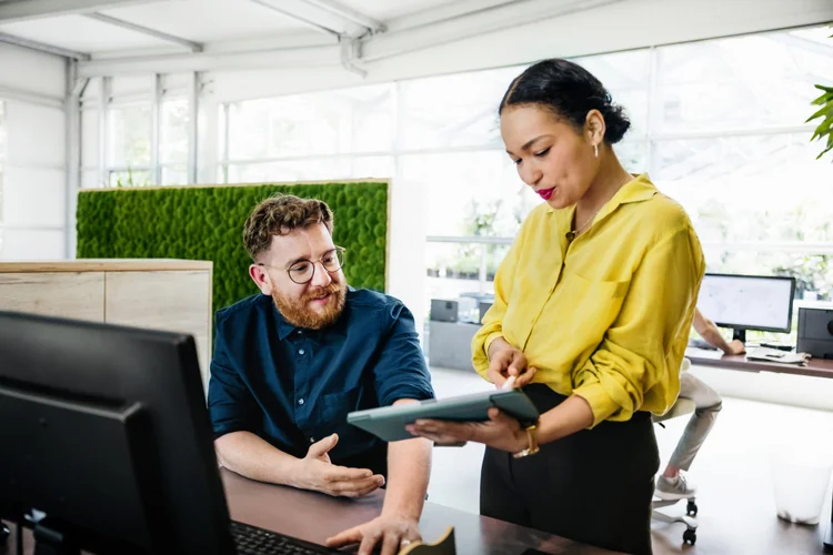 An office manager showing some documents on a digital tablet to her colleague in a bright, modern office space.