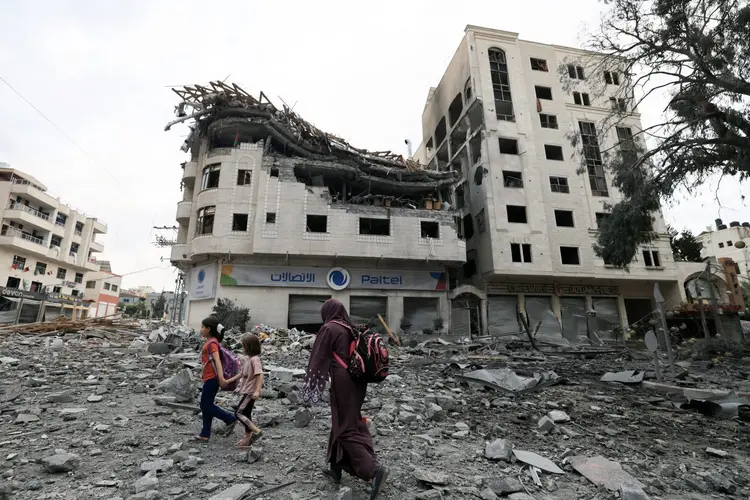 Ataques em Gaza: palestinos caminham perto de prédio destruído por ataque no distrito de al-Rimal ( Mahmud Hams/AFP)
