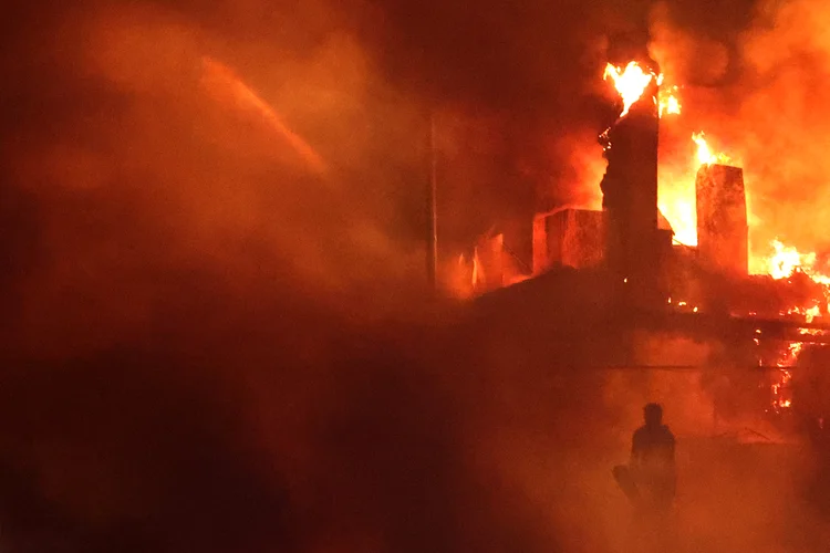 A Lebanese protester sits outside the US embassy as a fire rages behind its gates after clashes with Lebanese security forces on October 18, 2023, during a demonstration in solidarity with the people of Gaza in Awkar, East of Beirut, following a blast ripped through a hospital in the Gaza Strip, killing at least 200 people on October 17, 2023. The Israeli army said on October 17 a strike which hit a Gaza hospital, killing at least 200 people according to Hamas officials, was a rocket misfired by Palestinian militants. Lebanon's Iran-backed Hezbollah movement called for a "day of rage" to condemn the strike as hundreds of demonstrators gathered at the French and US embassies in protest. (Photo by JOSEPH EID / JOSEPH EID) (JOSEPH EID/AFP)