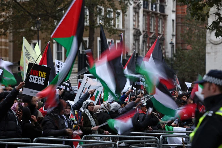 Manifestantes erguem cartazes e agitam bandeiras palestinas nos portões de Downing Street depois de participarem de uma Marcha pela Palestina, em Londres (AFP)