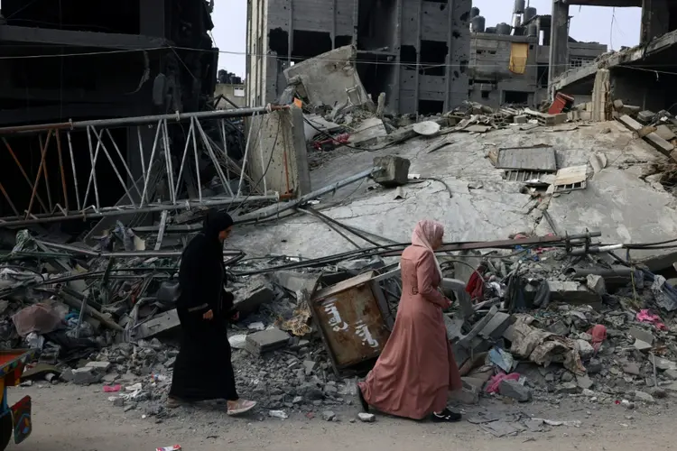 Uma mulher passa pelos escombros de um edifício em Rafah, sul da Faixa de Gaza, sob bombardeio israelense, 28 de outubro de 2023 (Adel ZAANOUN con Jonah MANDEL en Jerusalén/AFP)