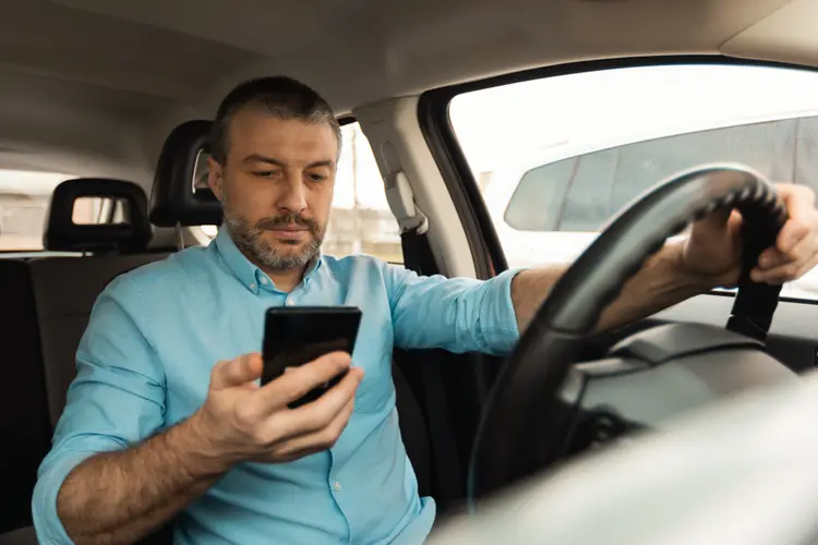 Male Driver Using Smartphone For Navigation Driving New Car Sitting In Auto. Man Using Traffic Application On Cellphone Riding In City. Transportation And Technology.