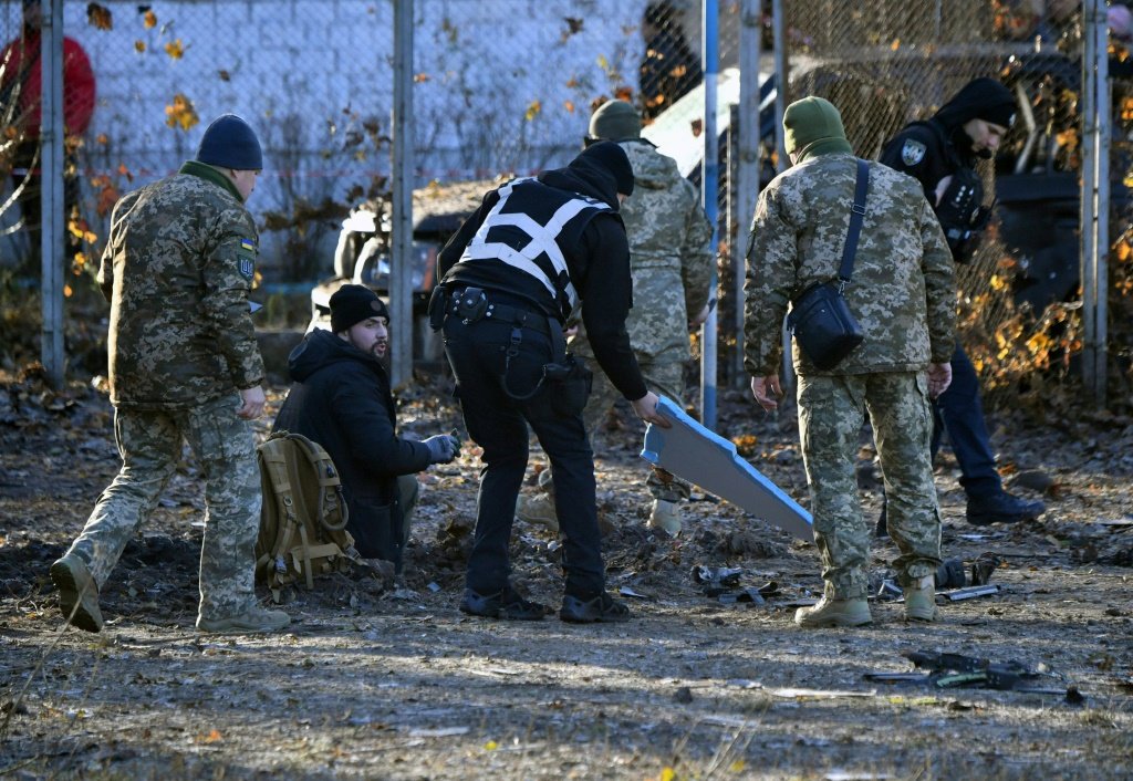 A polícia e os militares ucranianos coletam fragmentos de um drone russo abatido próximo ao buraco que deixou no pátio de alguns edifícios residenciais. (AFP/AFP Photo)