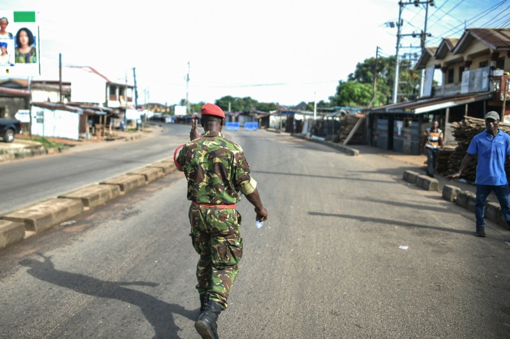 Um soldado da polícia militar de Serra Leoa cumprimenta um homem em uma rua bloqueada em Freetown, 26 de novembro de 2023 (AFP/AFP Photo)