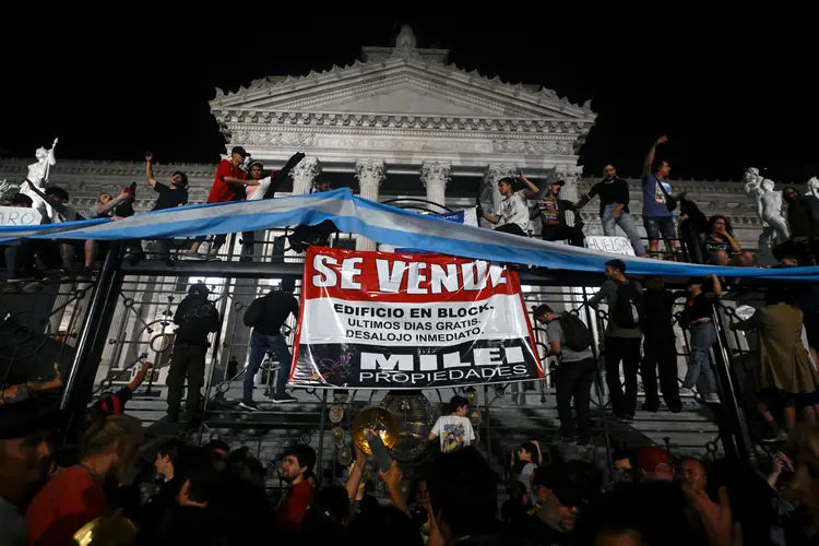 Manifestantes colam cartazes contra Milei nas grades do Congresso, durante protesto na quarta, 20 (Luis Robayo/AFP)