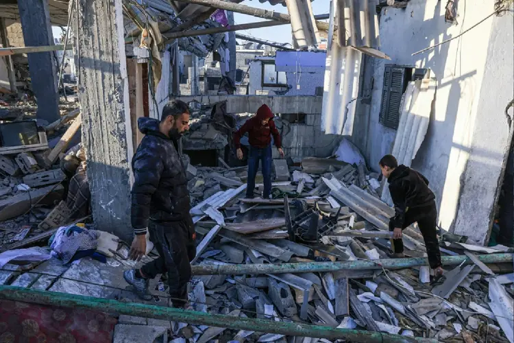 Palestinos caminham entre os escombors de prédio atingido por bombardeio israelense na Faixa de Gaza (Agence France-Presse/AFP Photo)