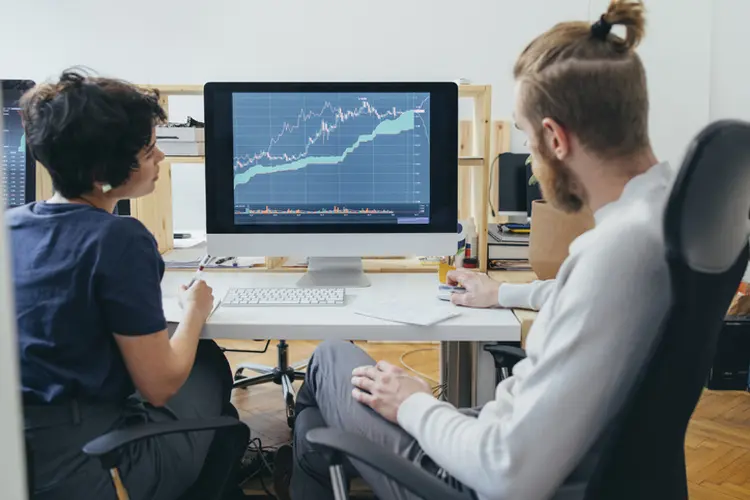Anonymous businesspeople analyzing a stock market investment graph together in the office (FreshSplash/Getty Images)