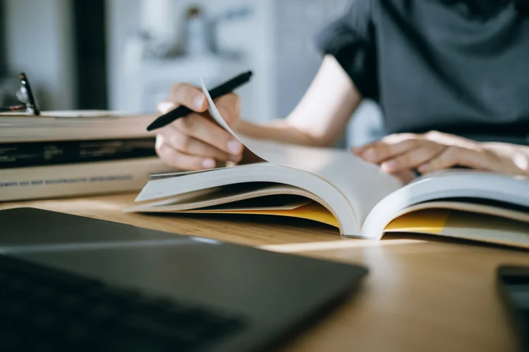 Close up. mid-section of young Asian woman reading book and making notes at home, concentrates on her studies. Further education concept (Divulgação: d3sign/Getty Images)