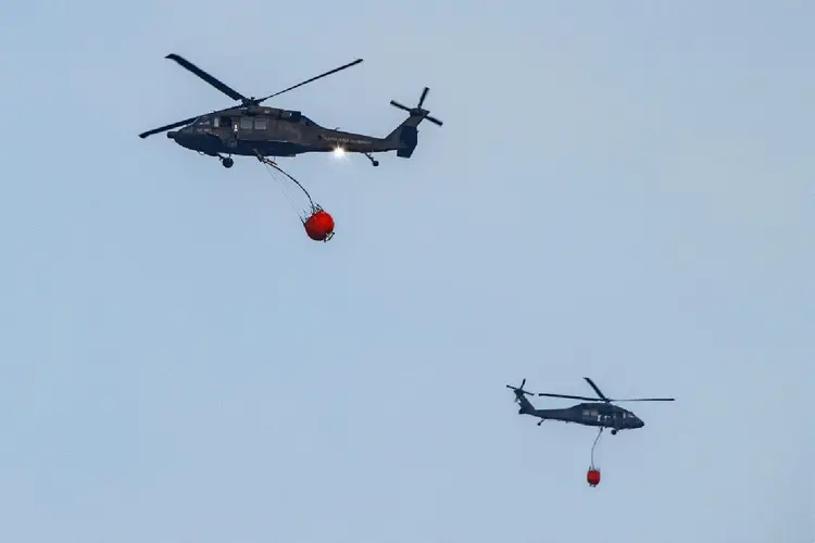 Helicópteros da polícia colombiana lançam água para combater incêndios florestais nas proximidades de Bogotá, em 24 de janeiro de 2024 (Agence France-Presse/AFP Photo)