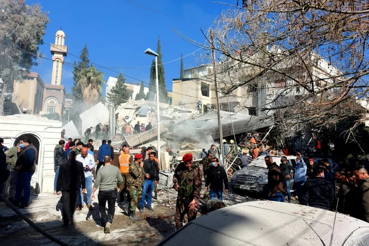 Populares e forças de segurança se reúnem em frente a um prédio destruído em um ataque israelense em Damasco, 20 de janeiro de 2024 (AFP/AFP)