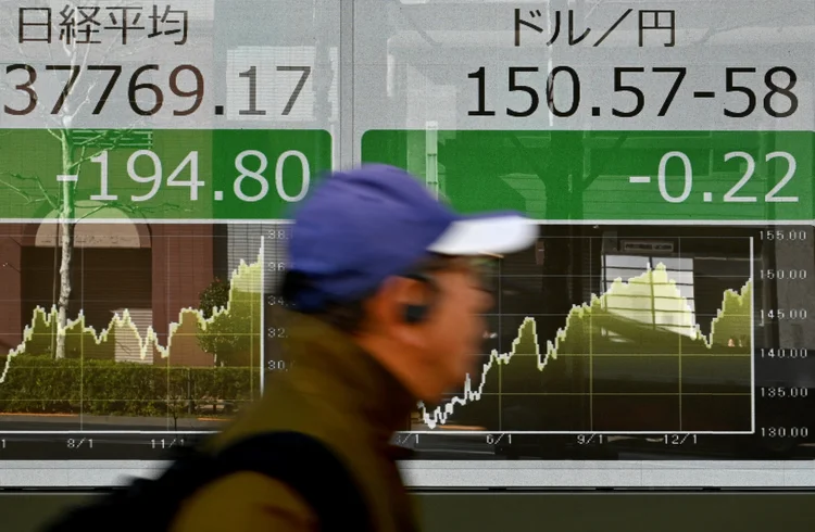 A pedestrian walks past an electronic board showing a share price of the Tokyo Stock Exchange (L) and the rate of the Japanese yen versus the US dollar (R) along a street in Tokyo on February 14, 2024. (Photo by Kazuhiro NOGI / AFP) (Photo by KAZUHIRO NOGI/AFP via Getty Images)