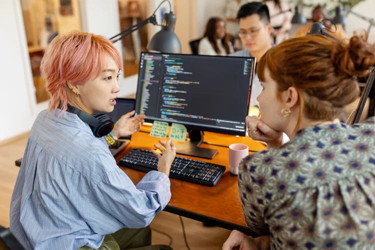 Female software developers discuss over the computer while sitting at a desk in the workplace. Creative businesswomen discuss the new coding program in the office. (Luiz Alvarez/Getty Images)