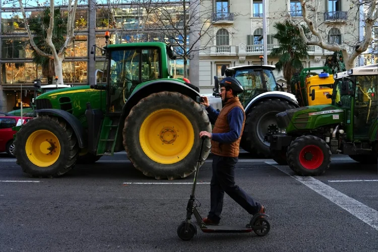 Pessoa passa de patinete em frente a uma fila de tratores concentrados em Barcelona em 7 de fevereiro de 2024 (Valentin Bontemps/AFP Photo)