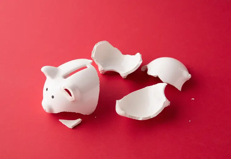 Broken whiter ceramic piggy bank in pieces on red surface (PM Images/Getty Images)