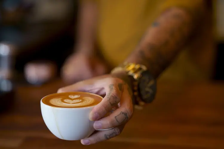 Barista hand serving a latte coffee cup has creative heart art design milk form on top (Getty Images/Reprodução)