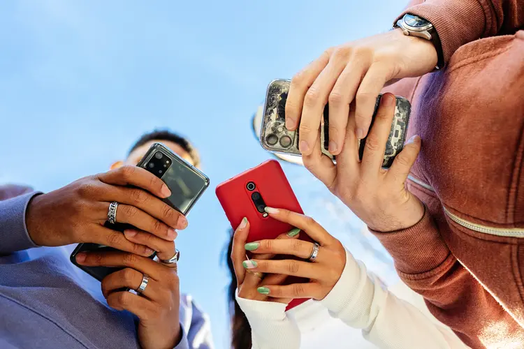 Grupo de três pessoas segura smartphones nas mãos. (Divulgação / Getty Images)