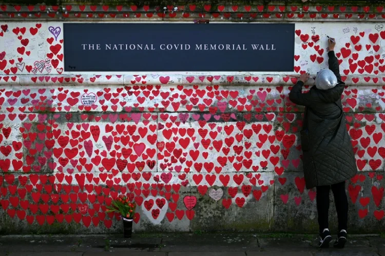 Uma pessoa escreve no National Covid Memorial Wall, dedicado àqueles que perderam suas vidas para a covid-19, na margem sul do rio Tâmisa, em Londres (Amélie BOTTOLLIER-DEPOIS/AFP)