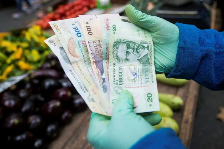 Um vendedor de frutas e verduras exibe notas de pesos uruguaios em uma feira de rua em Montevidéu (Alina Dieste/AFP)