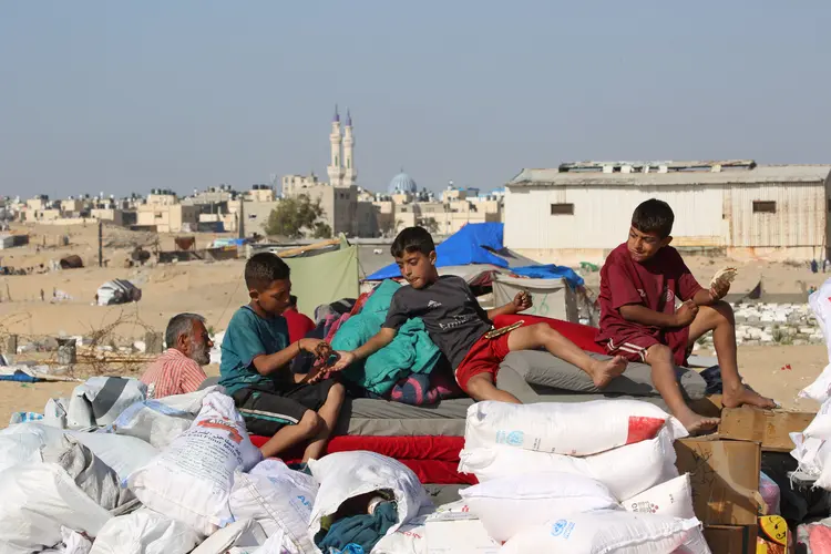 Crianças palestinas comem pão achatado em cima de um veículo carregado de pertences enquanto se preparam para fugir de Rafah, no sul da Faixa de Gaza, em direção a uma área mais segura, em 12 de maio de 2024, em meio ao conflito em curso entre Israel e o grupo militante Hamas (Divulgação/AFP)