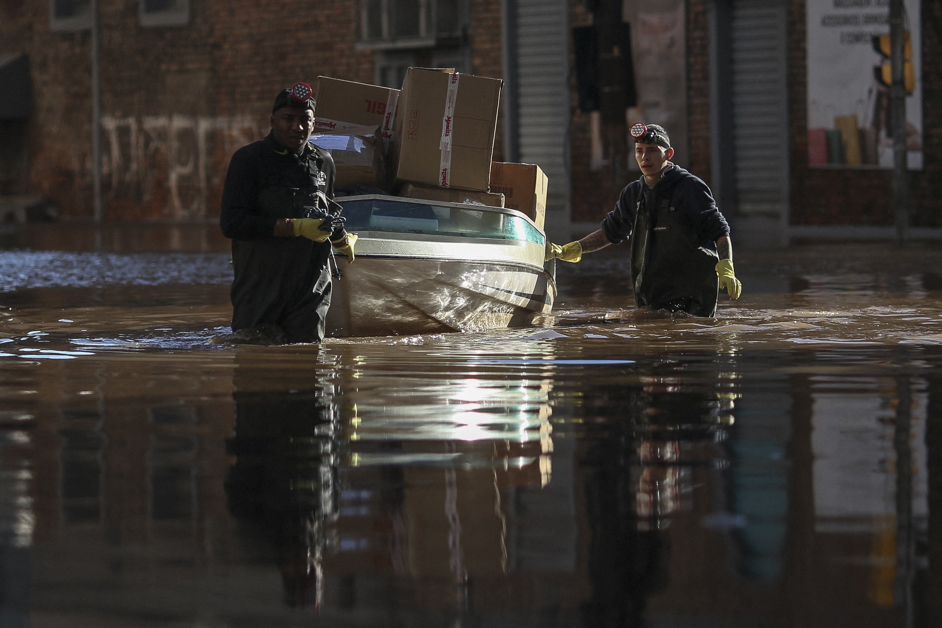 Homens movem pacotes em um barco através de uma rua inundada no centro histórico de Porto Alegre