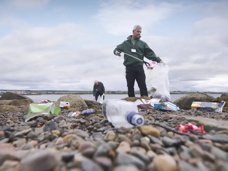 Lixo: homens limpam areia à beira-mar, lotada de garrafas plásticas (Getty Images)