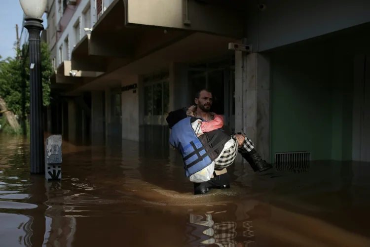 Brasil: voluntário leva uma senhora, de 79 anos, por uma rua inundada no bairro Cidade Baixa, em Porto Alegre (AFP Photo)