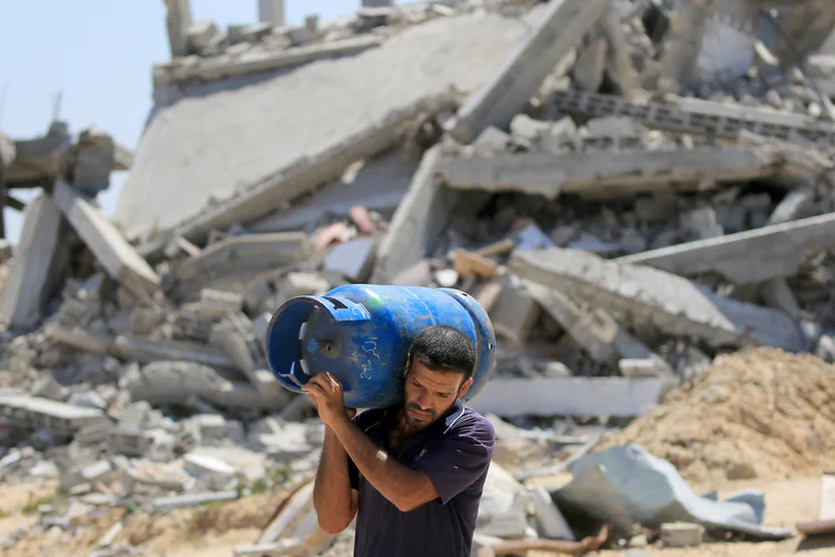 A Palestinian man walks carrying a gas bottle on his shoulder past buildings destroyed in the Israeli bombardment of Khan Yunis, in the southern Gaza Strip on June 11, 2024, amid the ongoing conflict between Israel and the Palestinian Hamas militant group. (Photo by Eyad BABA / AFP) (Eyad BABA/AFP)