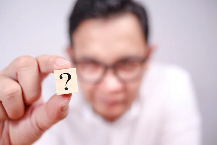 Close up image of businessman showing wooden block with question mark on it, selective focus (AdobeStock)