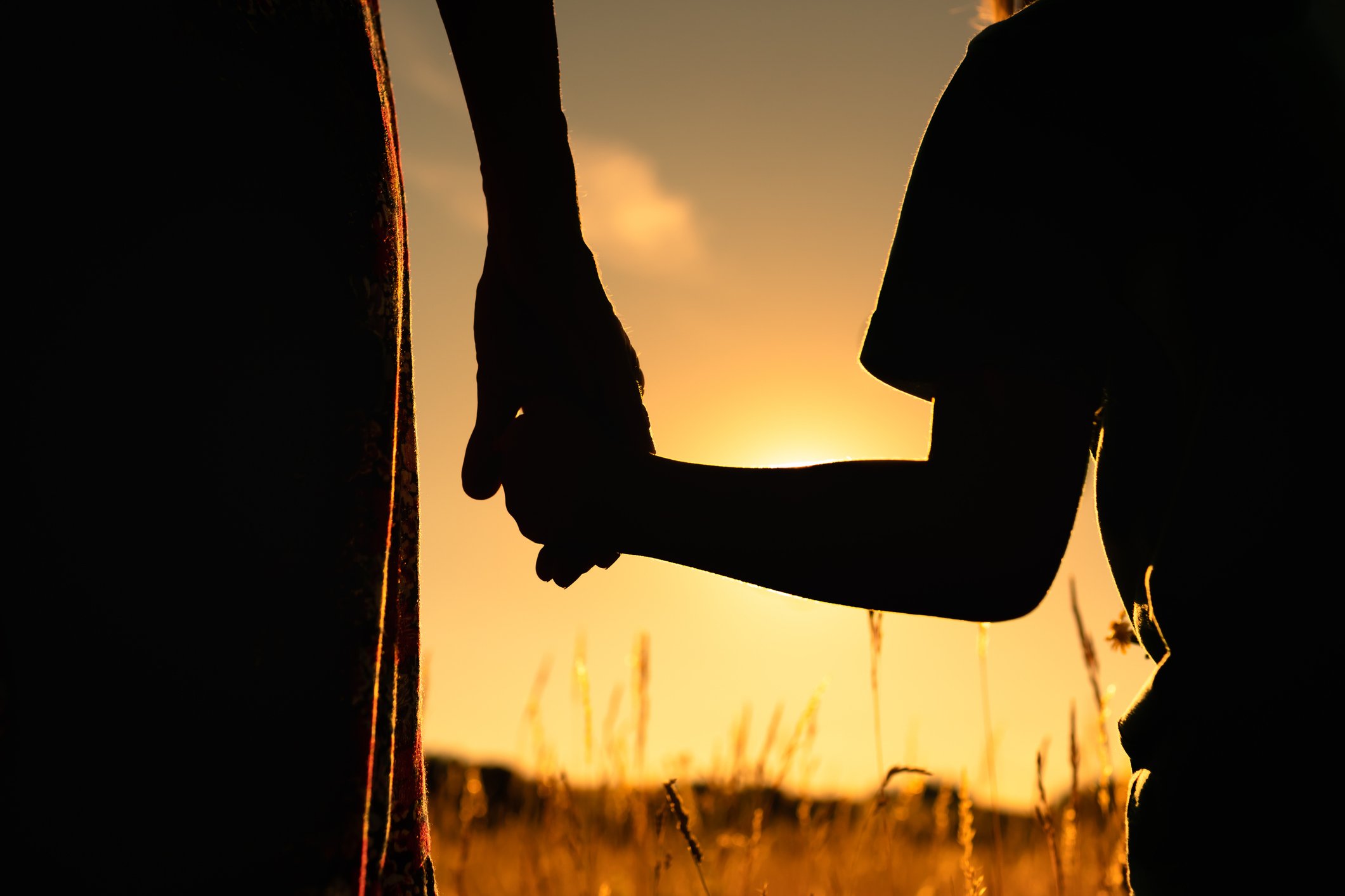 Silhouette of mother and child holding hands facing the sunset.