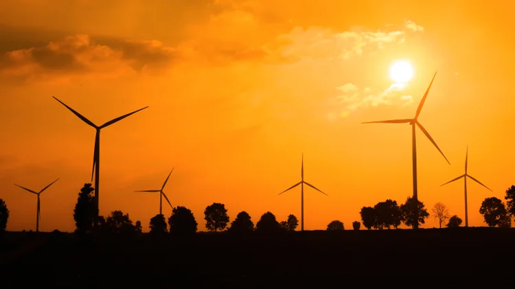 Electric wind turbines farm silhouettes on sun background. (wathanyu/Getty Images)