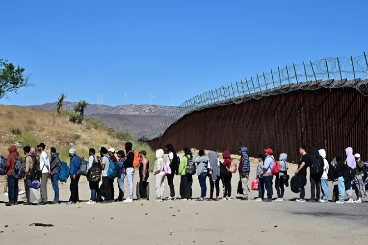 Um grupo de migrantes espera na fila da fronteira entre os EUA e o México, em Jacumba Hot Springs, Califórnia, em 5 de junho de 2024 (Paula RAMON/AFP)