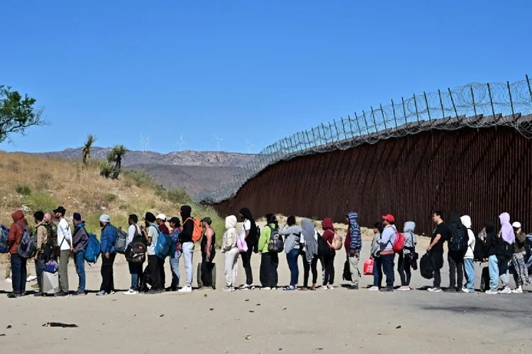 Um grupo de migrantes espera na fila da fronteira entre os EUA e o México, em Jacumba Hot Springs, Califórnia, em 5 de junho de 2024 (Paula RAMON/AFP)