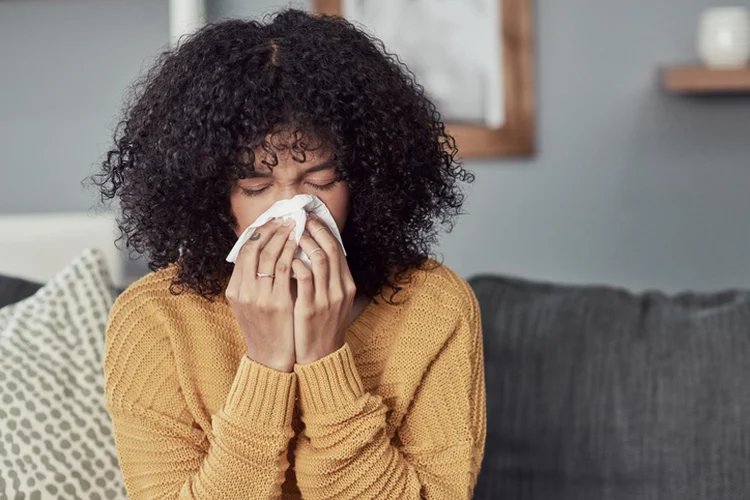 Shot of a young woman blowing her nose with a tissue at home (LaylaBird/Getty Images)