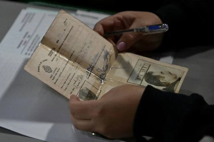 Um delegado segura a credencial de voto do ex-presidente uruguaio José Mujica enquanto ele vota em uma seção eleitoral durante as eleições primárias em Montevidéu. (AFP/AFP Photo)