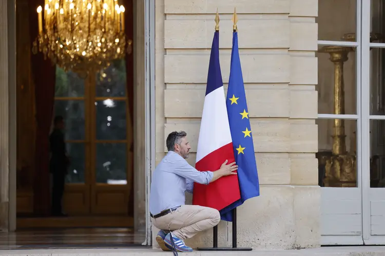 Homem arruma bandeiras francesa e da UE na frente do escritório do premiê francês (Foto: AFP)
