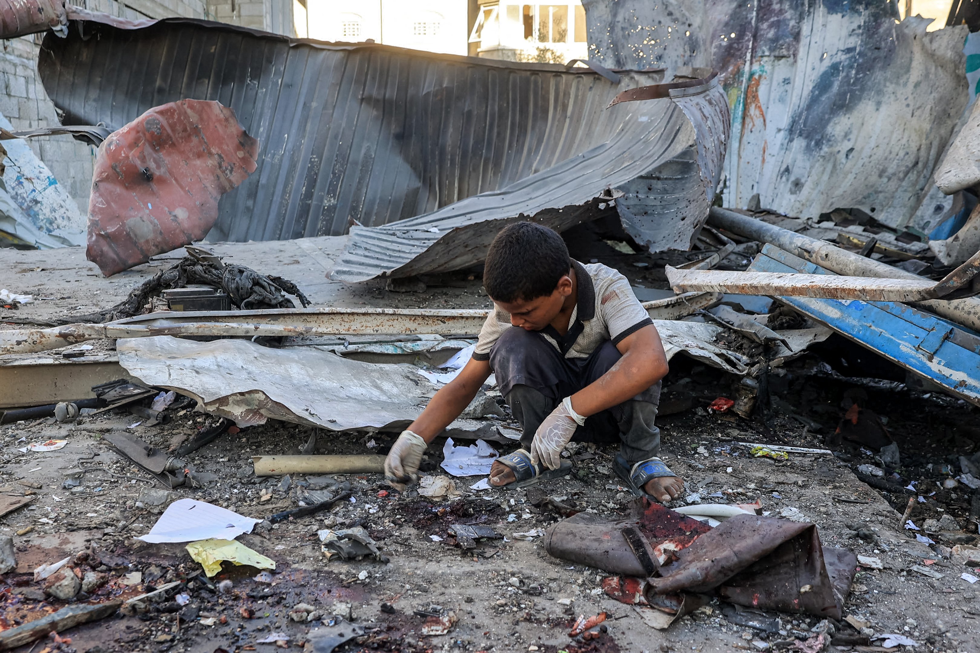 Um menino inspeciona os escombros de um prédio desabado após um bombardeio israelense na escola Jaouni, administrada pela Agência das Nações Unidas de Assistência aos Refugiados da Palestina (UNRWA), em Nuseirat, na região central da Faixa de Gaza, em 6 de julho de 2024, em meio ao conflito contínuo no território palestino entre Israel e o Hamas. (Foto de Eyad BABA / AFP)