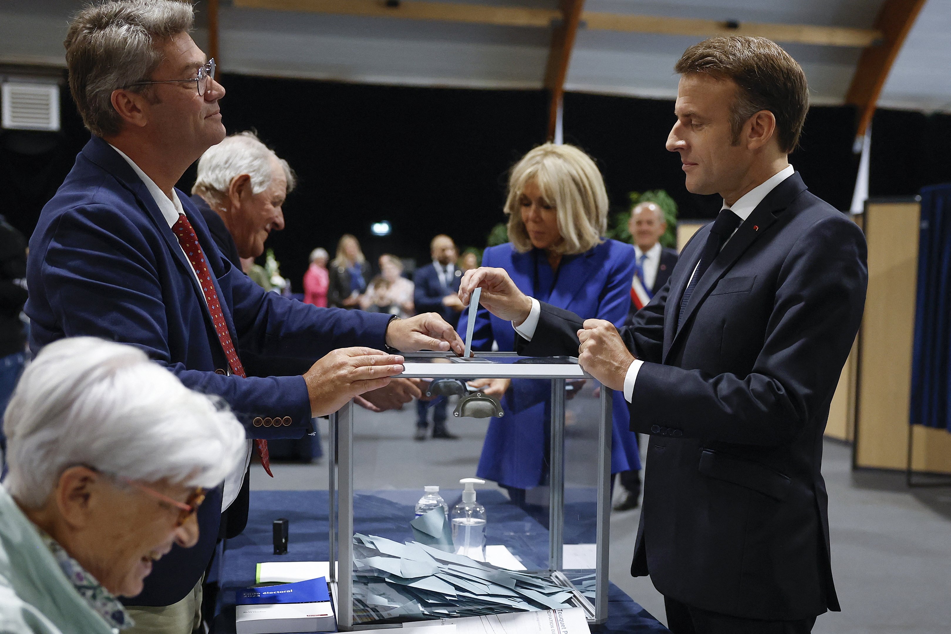 O presidente da França, Emmanuel Macron (à direita), acompanhado por sua esposa Brigitte Macron (no centro), deposita seu voto no segundo turno das eleições legislativas da França em um local de votação em Le Touquet, norte da França, em 7 de julho de 2024