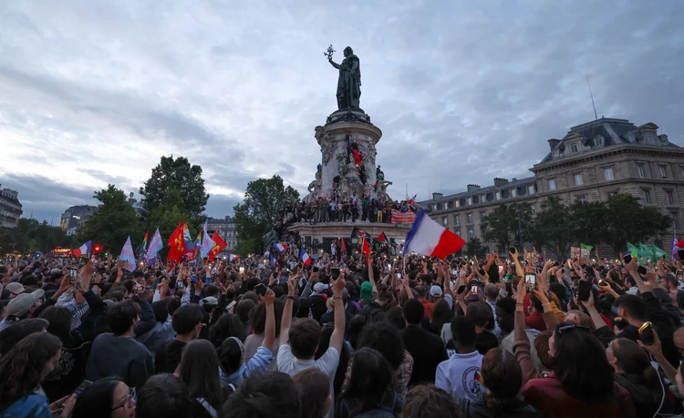 Os participantes acenam com os tricolores nacionais franceses durante um comício noturno eleitoral após os primeiros resultados do segundo turno das eleições legislativas da França na Place de la Republique, em Paris, em 7 de julho de 2024 (Emmanuel Dunand/AFP)