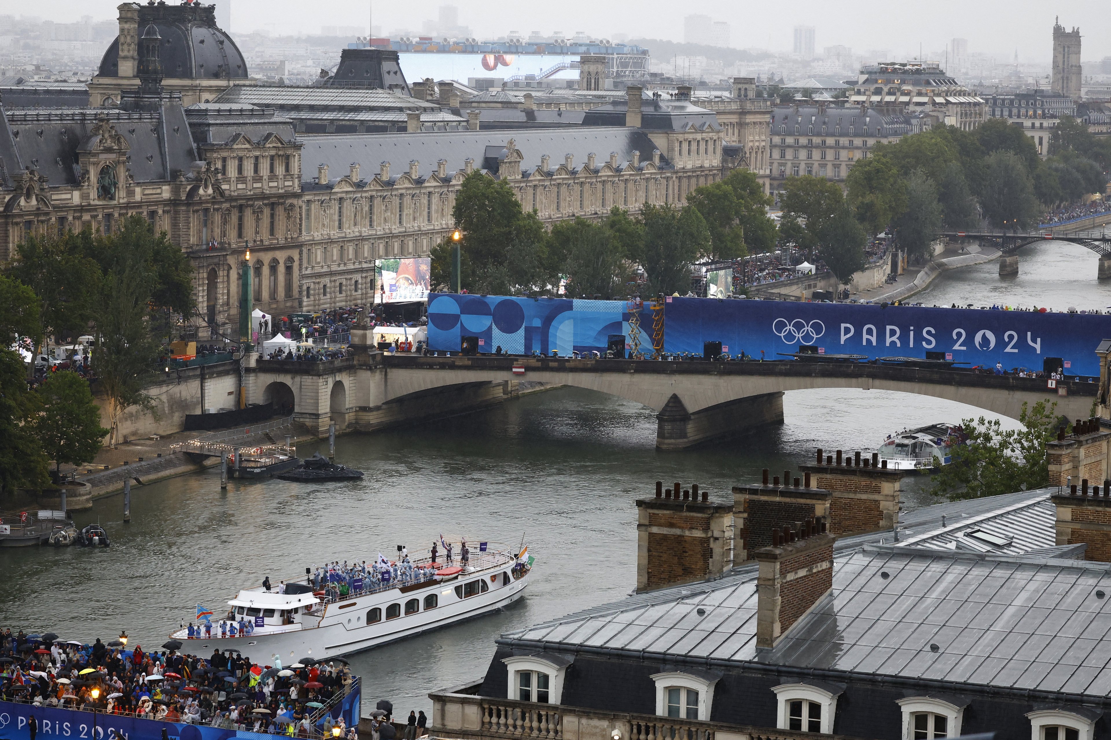 Atletas da Coreia do Sul, Costa do Marfim, Costa Rica e República Democrática do Congo a bordo de um barco no desfile flutuante passam pelo Museu do Louvre no rio Sena durante a cerimônia de abertura.