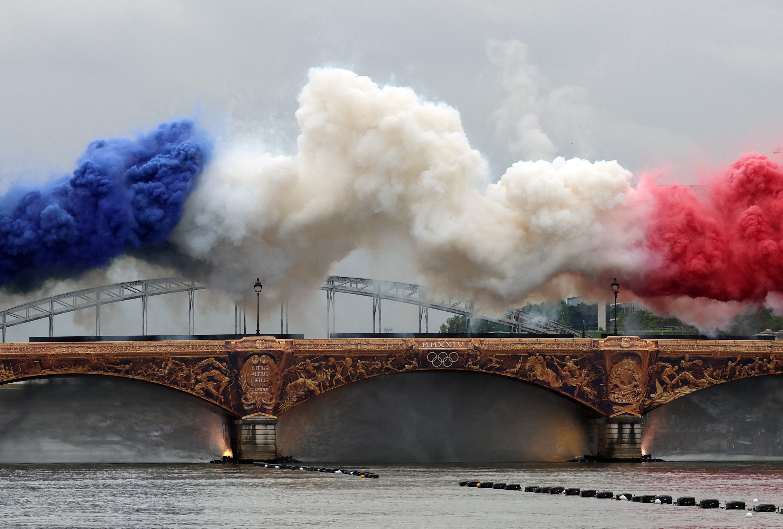 Coloured smoke forms the French flag on the Austerlitz bridge over the river Seine at the start of the opening ceremony of the Paris 2024 Olympic Games in Paris on July 26, 2024. (Photo by Emmanuel DUNAND / AFP)