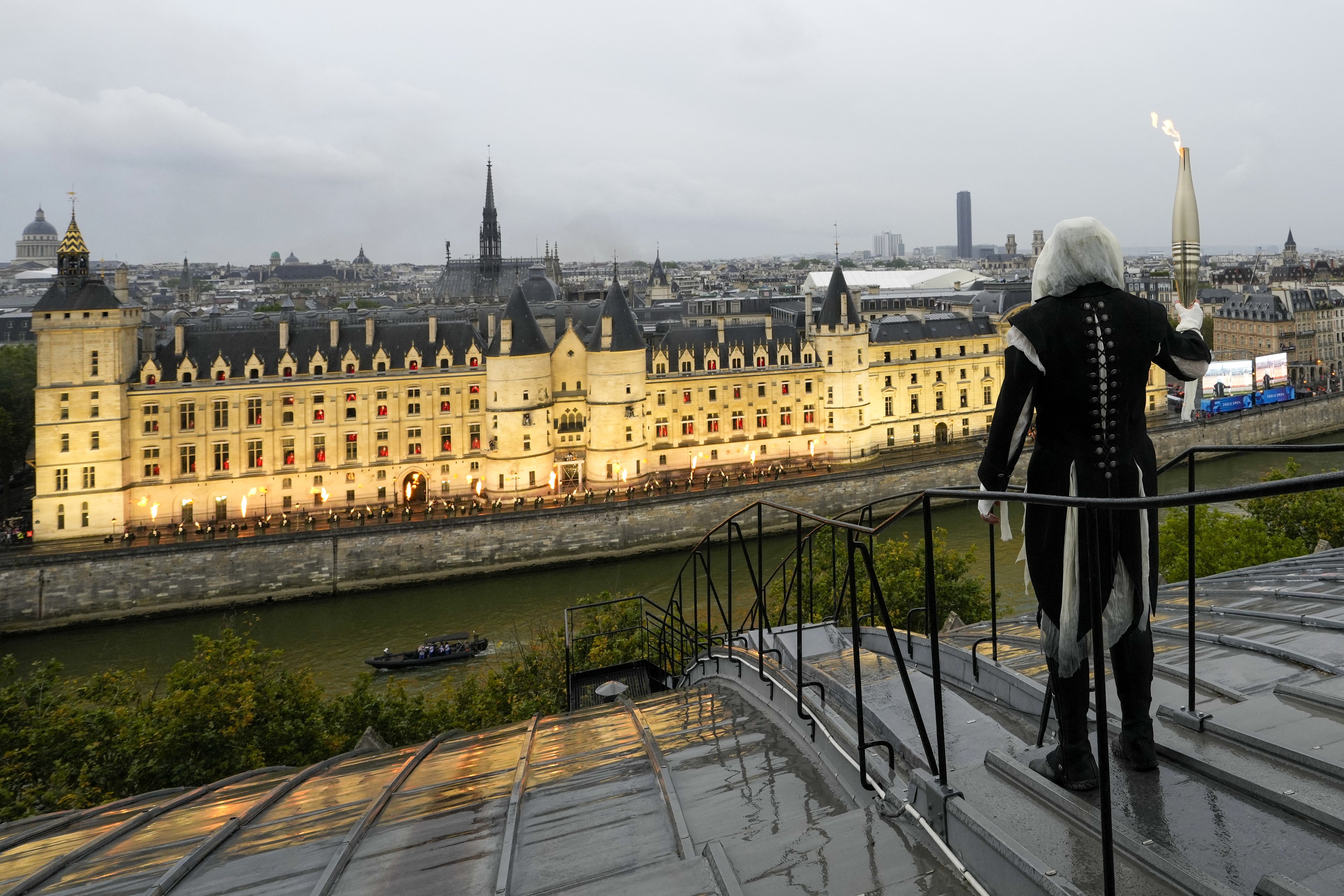 Um portador da tocha carrega a chama olímpica sobre um prédio ao longo do Rio Sena em Paris, França, durante a cerimônia de abertura dos Jogos Olímpicos de Verão de 2024