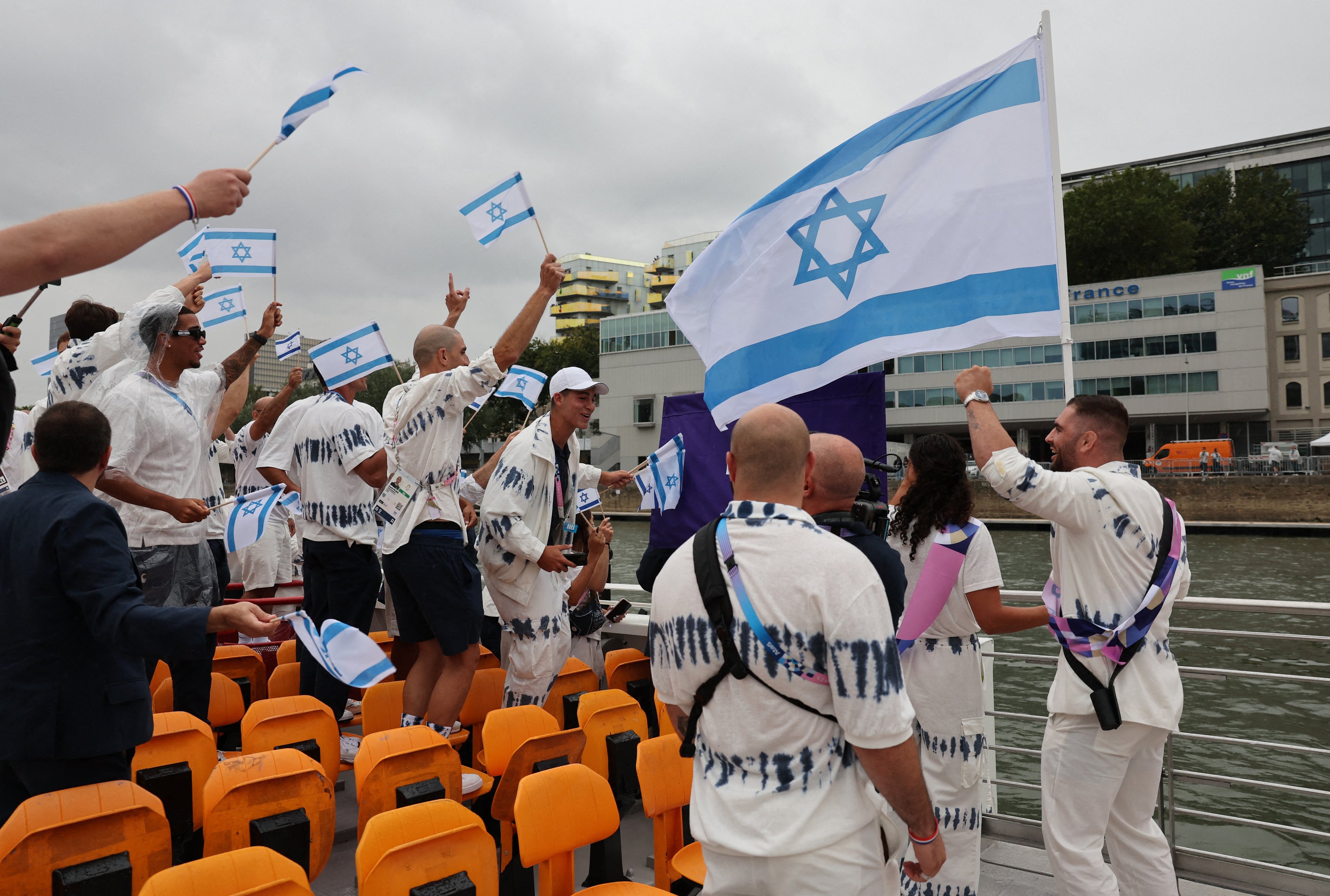 Atletas de Israel, incluindo os porta-bandeiras Andrea Murez e Peter Paltchik, são vistos a bordo de um barco no desfile flutuante no rio Sena durante a cerimônia de abertura